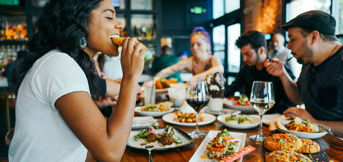 Friends leaning over a crowded table of shared plates, mid-conversation.