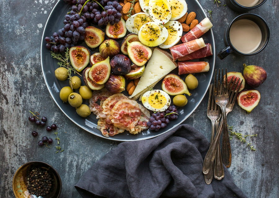 Figs, olives, jammy eggs and aged cheese arranged on dark slate under low light.