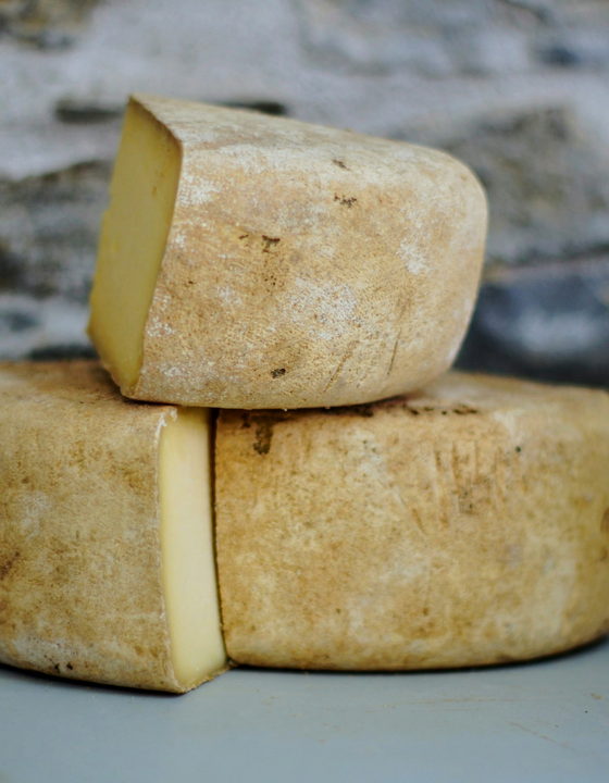 Stacked wheels of aged cheese resting on a stone shelf in a cellar.