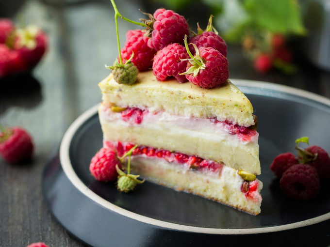 A slice of raspberry layer cake on a dark plate under warm light.